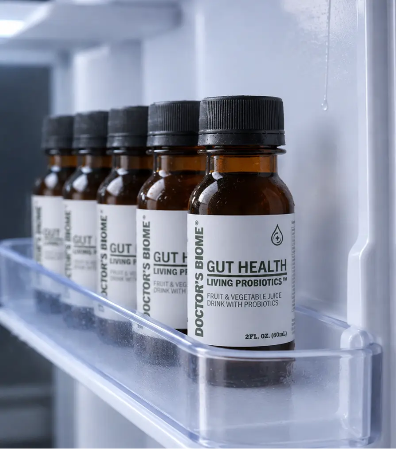 Six bottles of Doctor's Biome Gut Health standing in a row on a refrigerator door shelf, condensation on the glass.