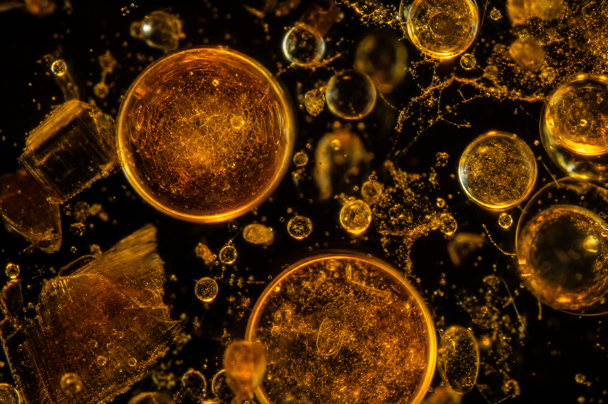 Glowing amber and gold droplets and fine particles suspended in dark liquid.